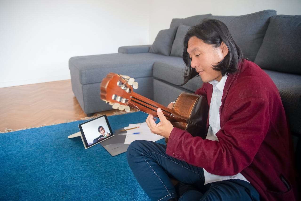 Hombre sentado tomando clases de guitarra online frente a un ordenador portátil, representando el aprendizaje y enseñanza musical a distancia.