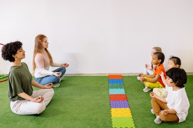 Dos instructoras especializadas en yoga infantil guían a cuatro niños en la postura del Loto
