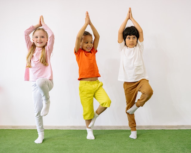 Tres niños felices practicando la postura del árbol en una clase de yoga para niños.
